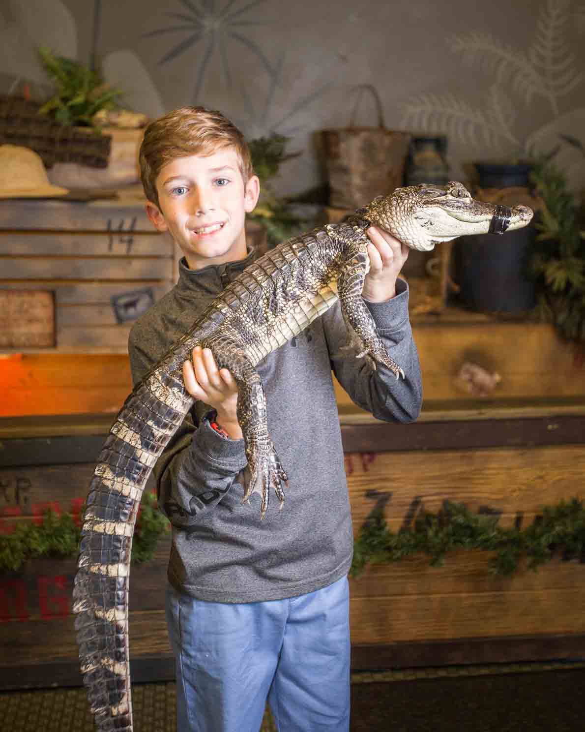 A boy holding an alligator in his hands.