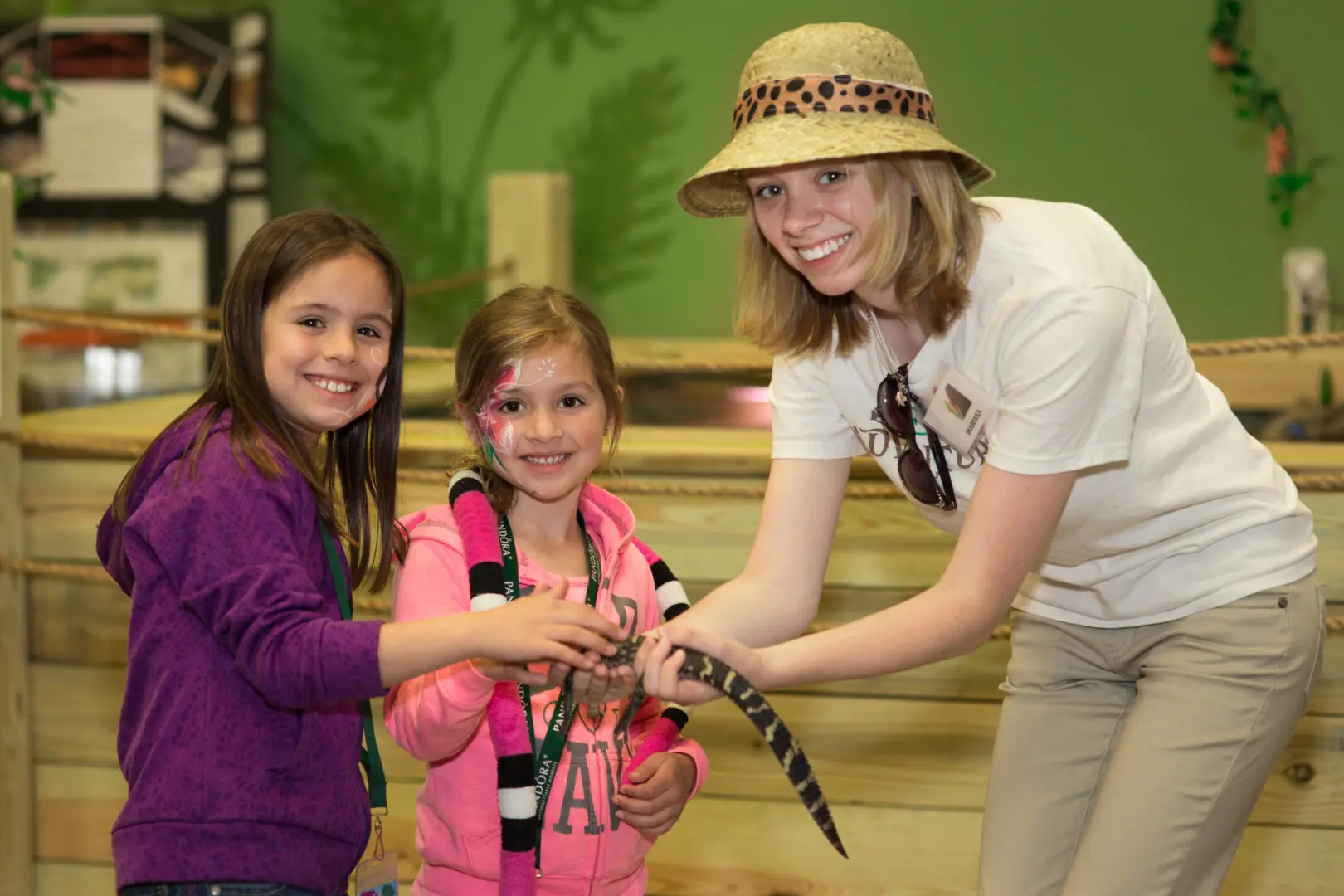 A woman holding a snake next to two girls.