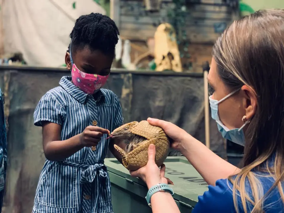 A woman wearing a mask is handing something to a child.