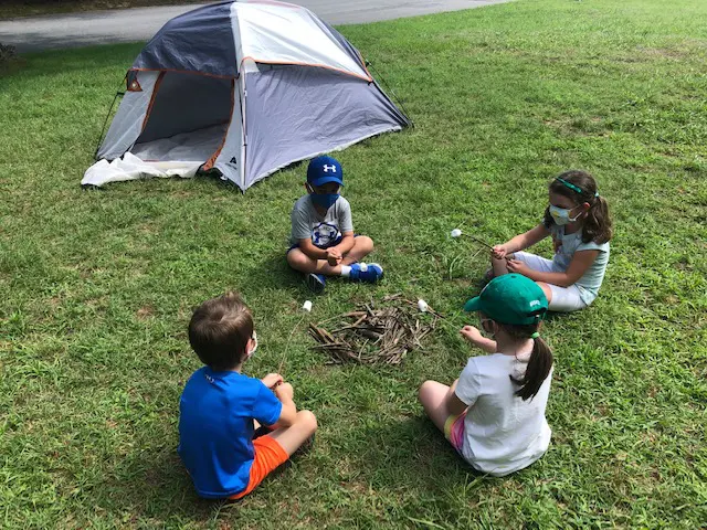 A group of kids sitting in the grass near a tent.