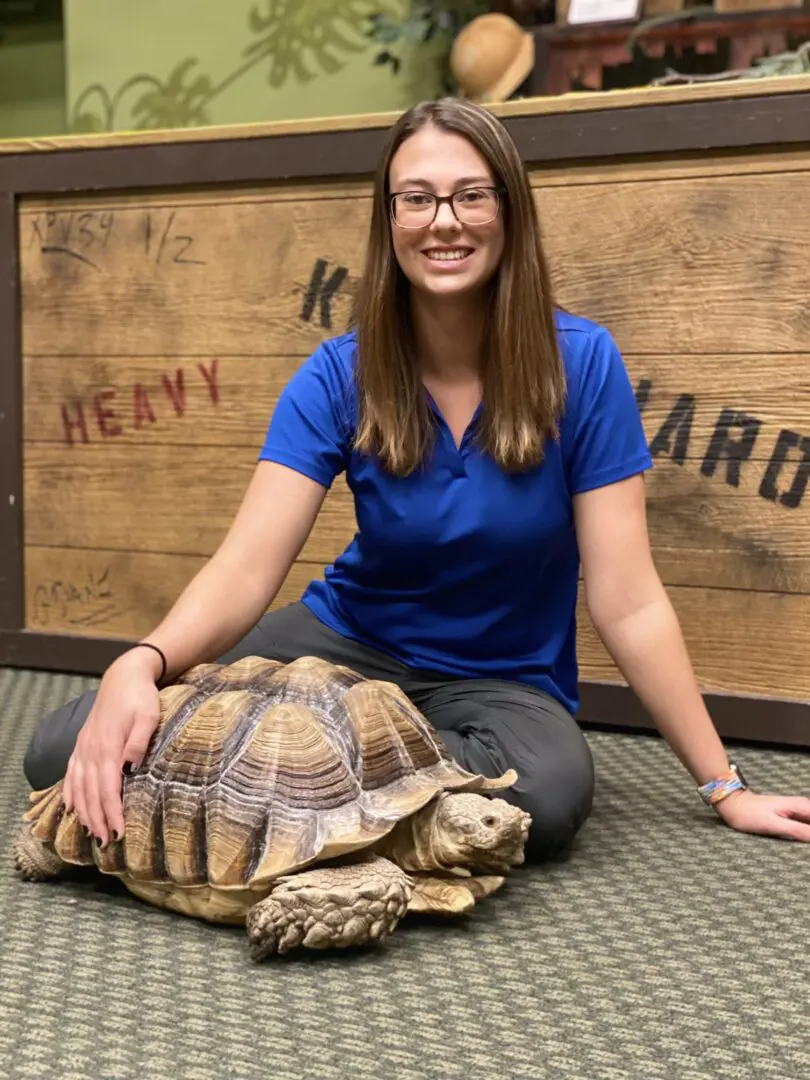 A woman sitting on the ground next to a turtle.