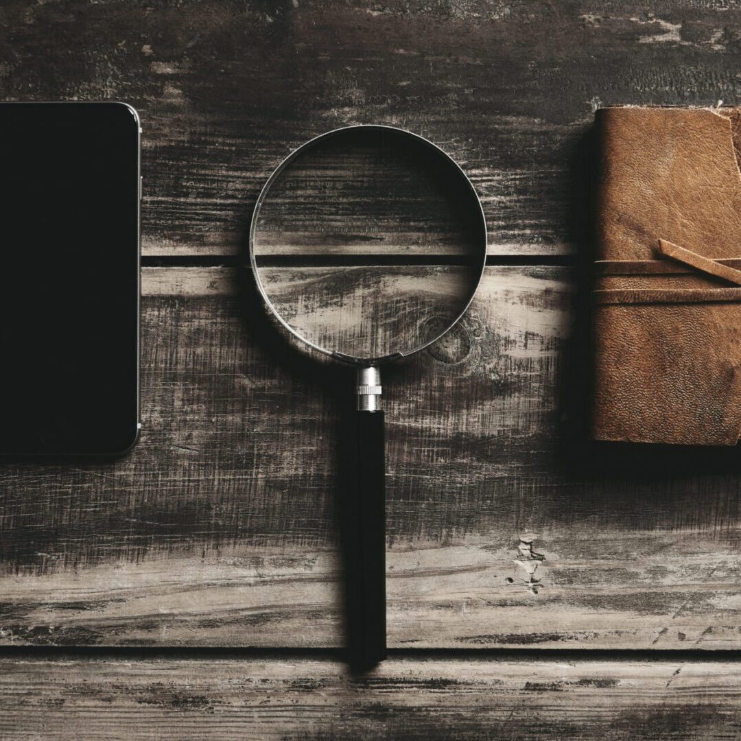 Mobile smartphone, magnifier and notebook with leather cover isolated on black farm wooden table Mysterious detective game concept.
