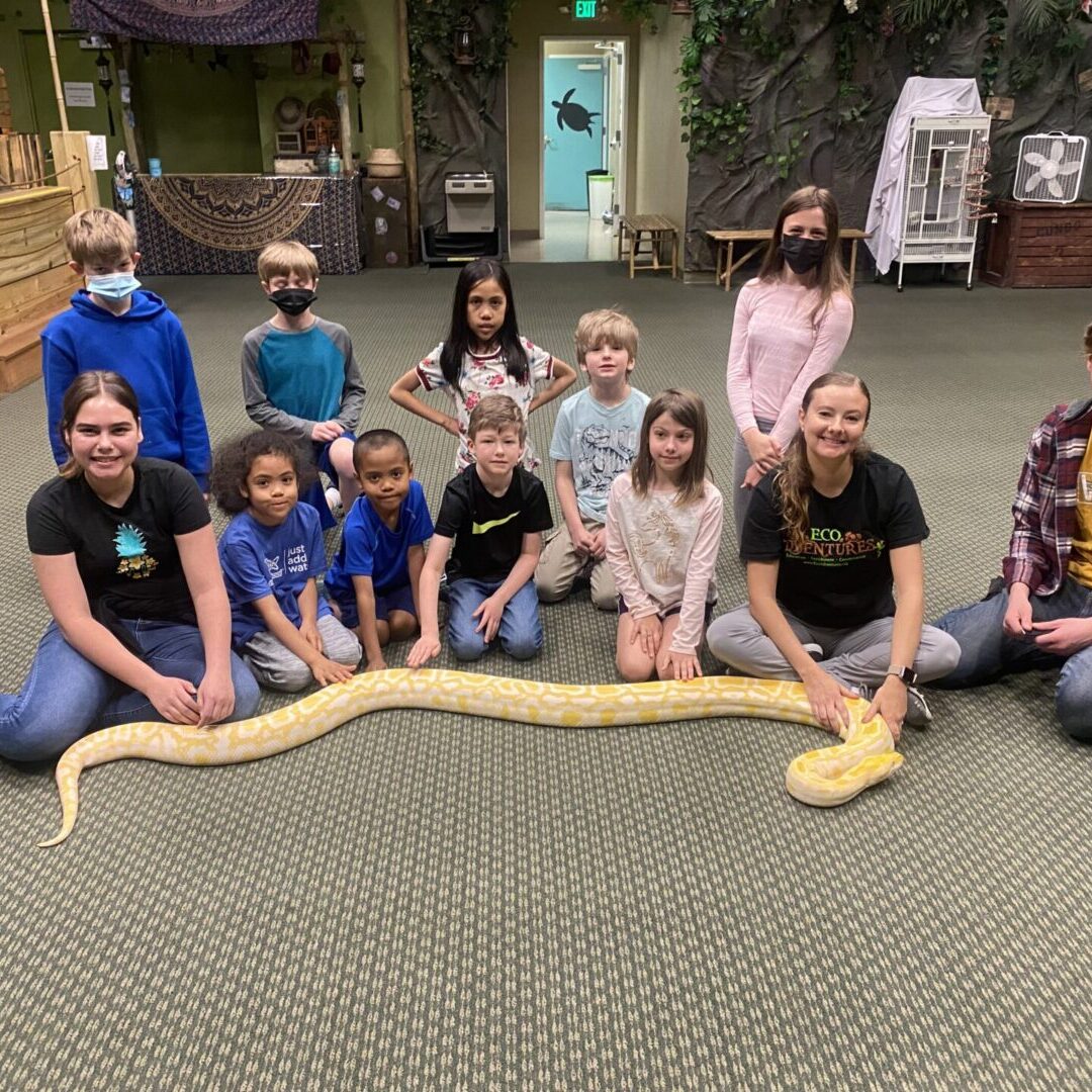 A group of people sitting around a snake.