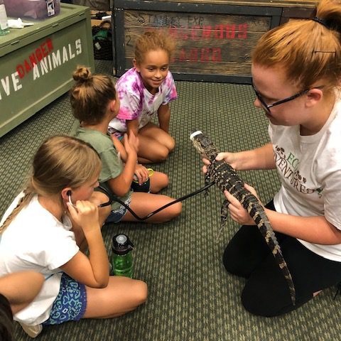 A group of girls sitting on the ground with a snake.